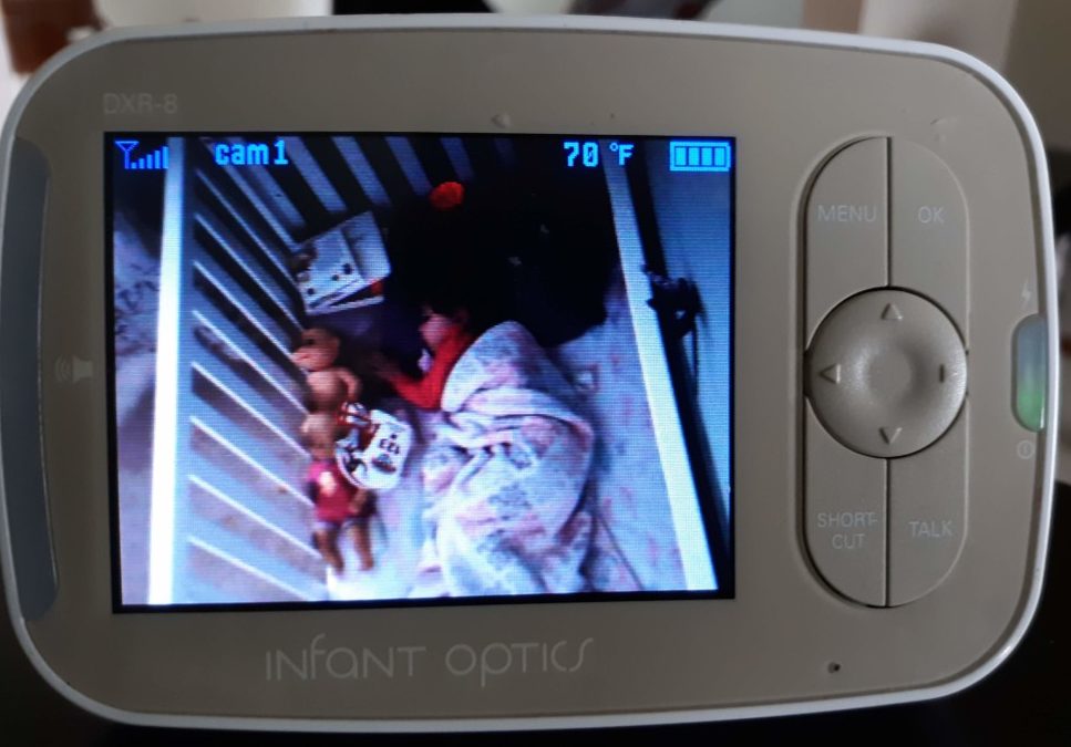 baby monitor showing toddler sleeping in crib with many items