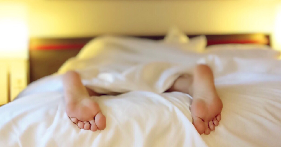 woman laying down on bed with feet sticking out of covers