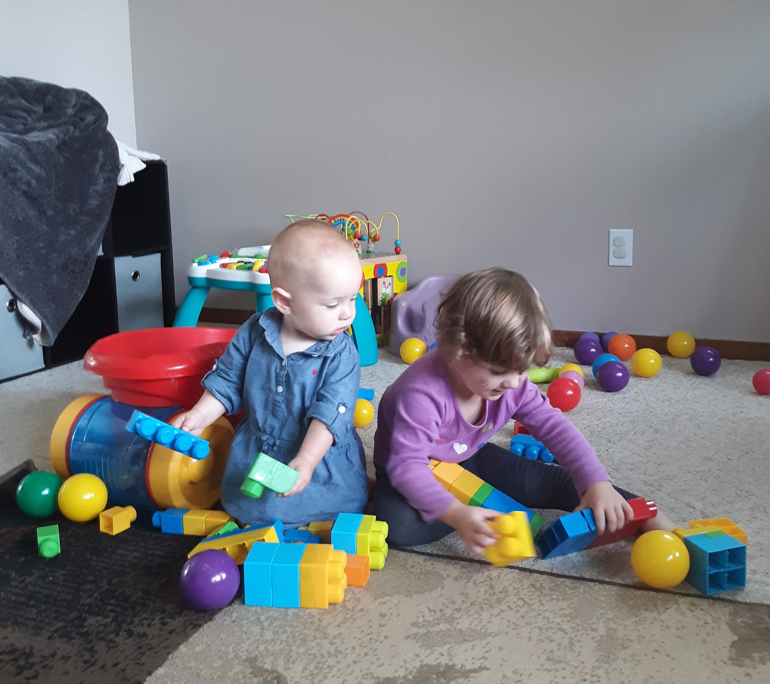 Toddlers playing with blocks and balls in a messy living room.
