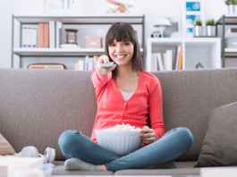 woman holding remote while sitting on a couch with popcorn in her lap