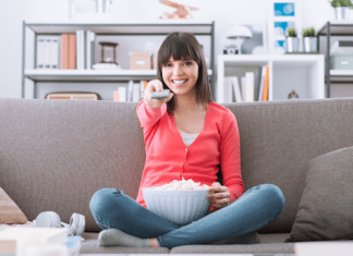 woman holding remote while sitting on a couch with popcorn in her lap