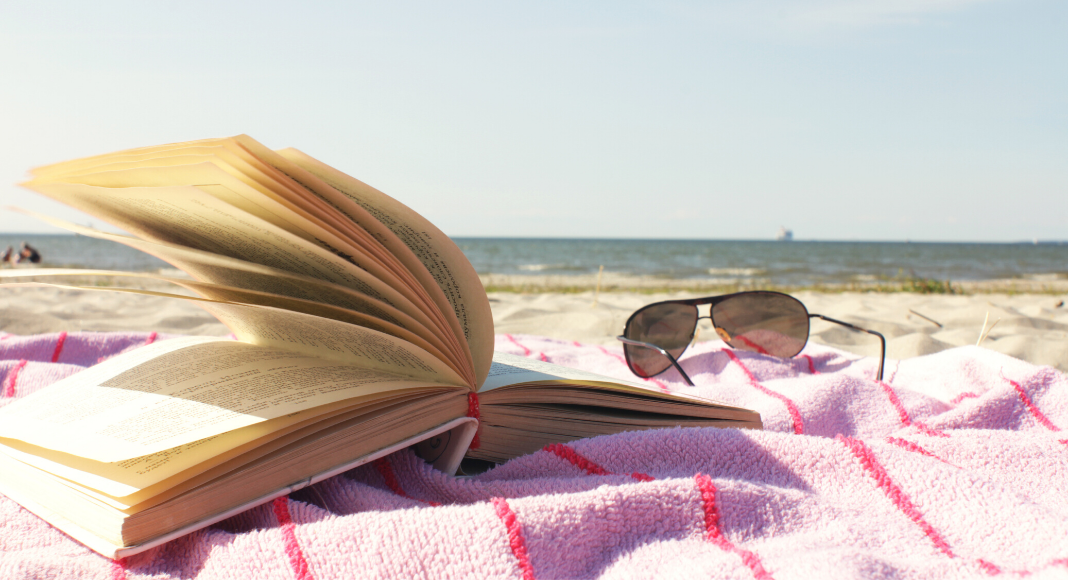 open book on beach towel next to sunglasses